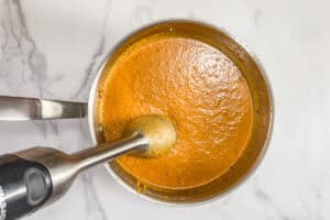 An immersion blender in a pot of butternut squash soup.