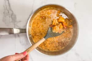 Butternut squash chunks, cream, stock, onions, and sun-dried tomatoes in a silver pot.
