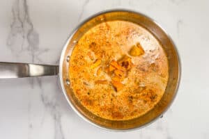 Cream, stock, butternut squash, spices, and sun-dried tomatoes in a silver pot.