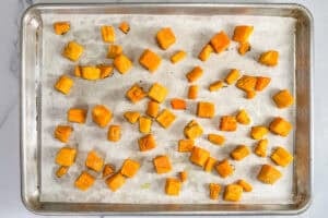 Roasted butternut squash chunks on a parchment lined sheet pan.