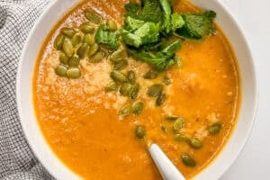 Marry me butternut squash soup topped with pepitas and parsley in a white bowl with a spoon.