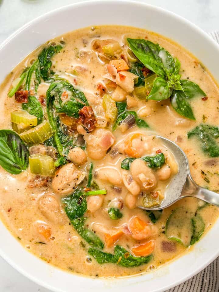 Marry me white bean soup with spinach in a white bowl with a silver spoon.