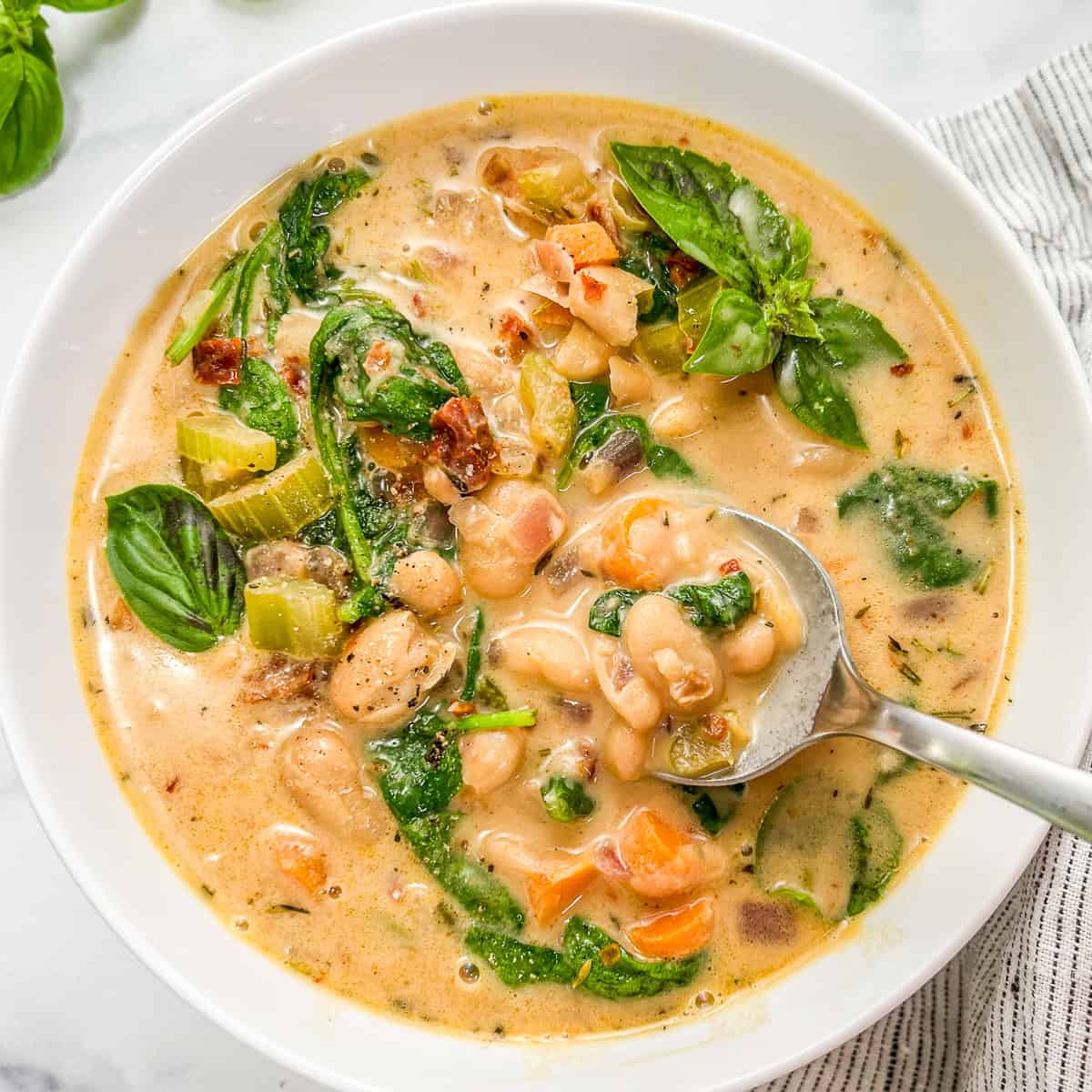 Marry me white bean soup with spinach in a white bowl with a silver spoon.