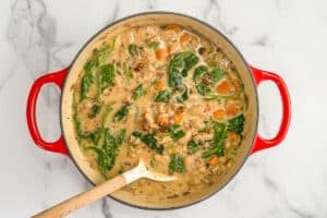 Marry me white bean soup with carrots, celery, sun-dried tomatoes, and spinach in a large red pot.