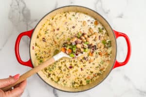 Beans and vegetables in a cream broth in a red pot.