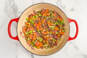 Sliced carrots, diced celery, and diced red onion cooking in a pot.
