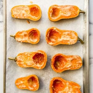 Halved honeynut squash covered with miso sauce on a parchment lined sheet pan.