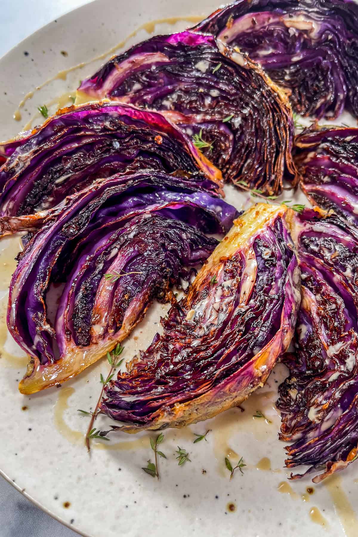 Roasted purple cabbage wedges drizzled with tahini on a speckled white plate.