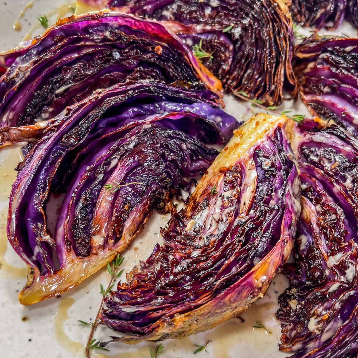 Roasted purple cabbage wedges drizzled with tahini on a speckled white plate.