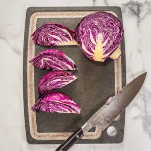 A halved cabbage cut into wedges on a black cutting board.