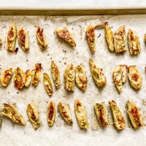 Baked artichoke hearts on a parchment lined sheet pan.