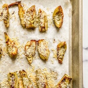 Artichoke hearts topped with parmesan on a sheet pan.