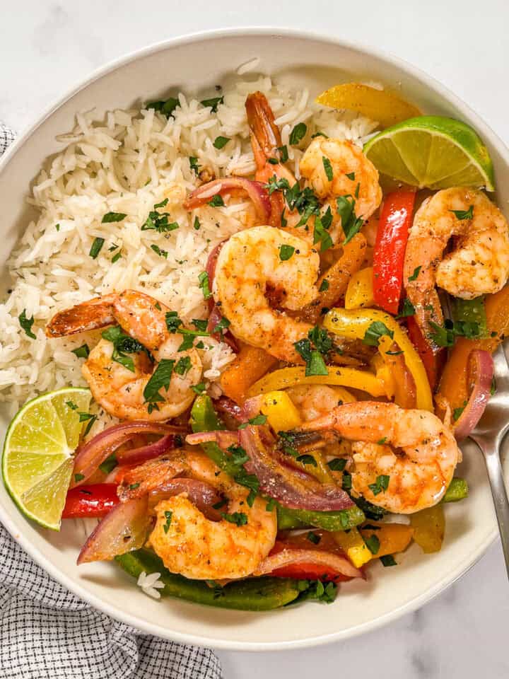 Sheet pan shrimp fajitas with white rice in a white bowl with a silver fork.