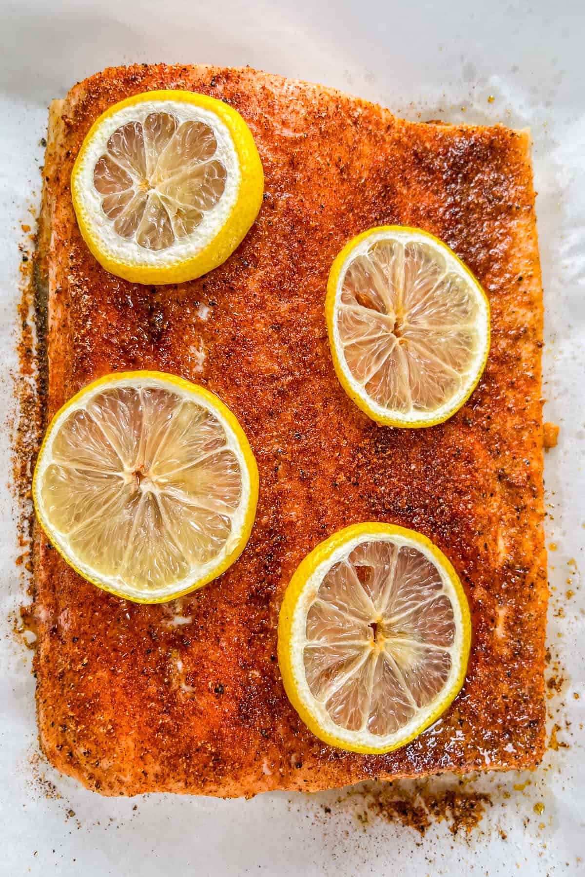 Slow roasted salmon topped with lemon slices on a piece of parchment.