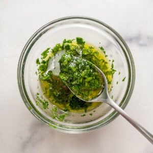 Cilantro, lemon, and olive oil being mixed in a small glass bowl.