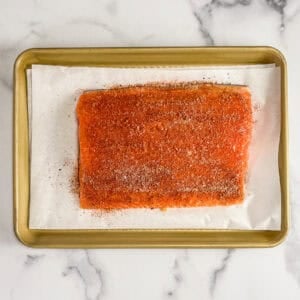 A salmon fillet topped with spices on a parchment lined sheet pan.