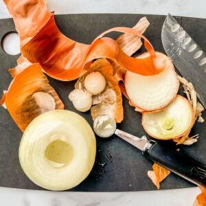 An onion being peeled and cored on a black cutting board.