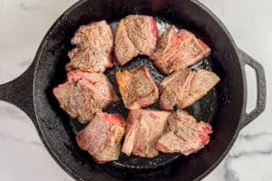 Chunks of beef being browned in a large cast iron pan.