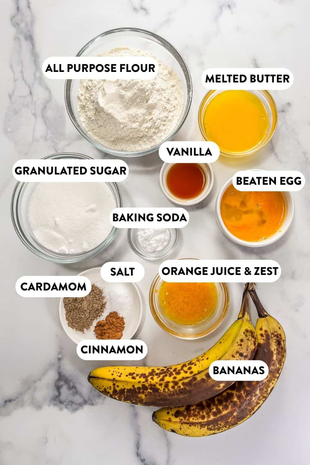 Ingredients for cardamom citrus banana bread on a marble background.
