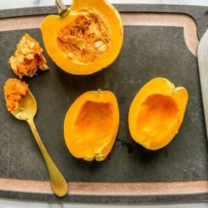 Carnival squash being cut into quarters on a black cutting board.