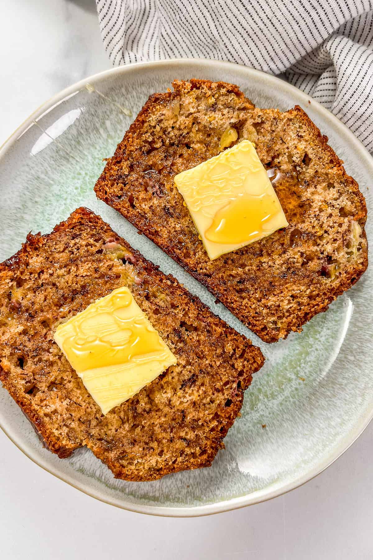 Two slices of cardamom banana bread topped with pats of butter and drizzled with honey on a small green plate.