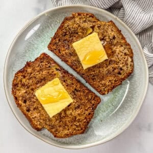 Two slices of cardamom banana bread topped with pats of butter and drizzled with honey on a small green plate.