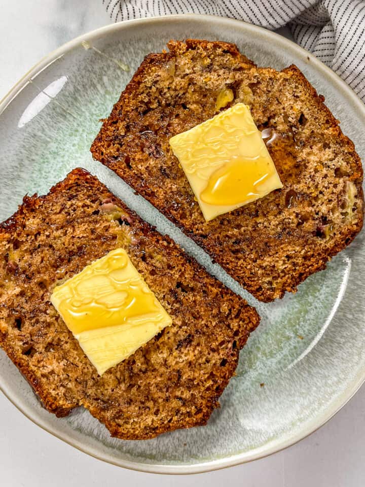 Two slices of cardamom banana bread topped with pats of butter and drizzled with honey on a small green plate.