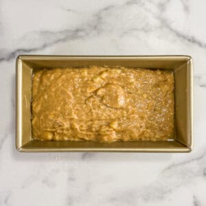 Cardamom banana bread batter in a gold loaf pan.