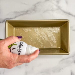 Spray oil being sprayed into a gold bread pan.