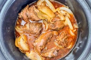 Beef barbacoa with sliced onions in a slow cooker.