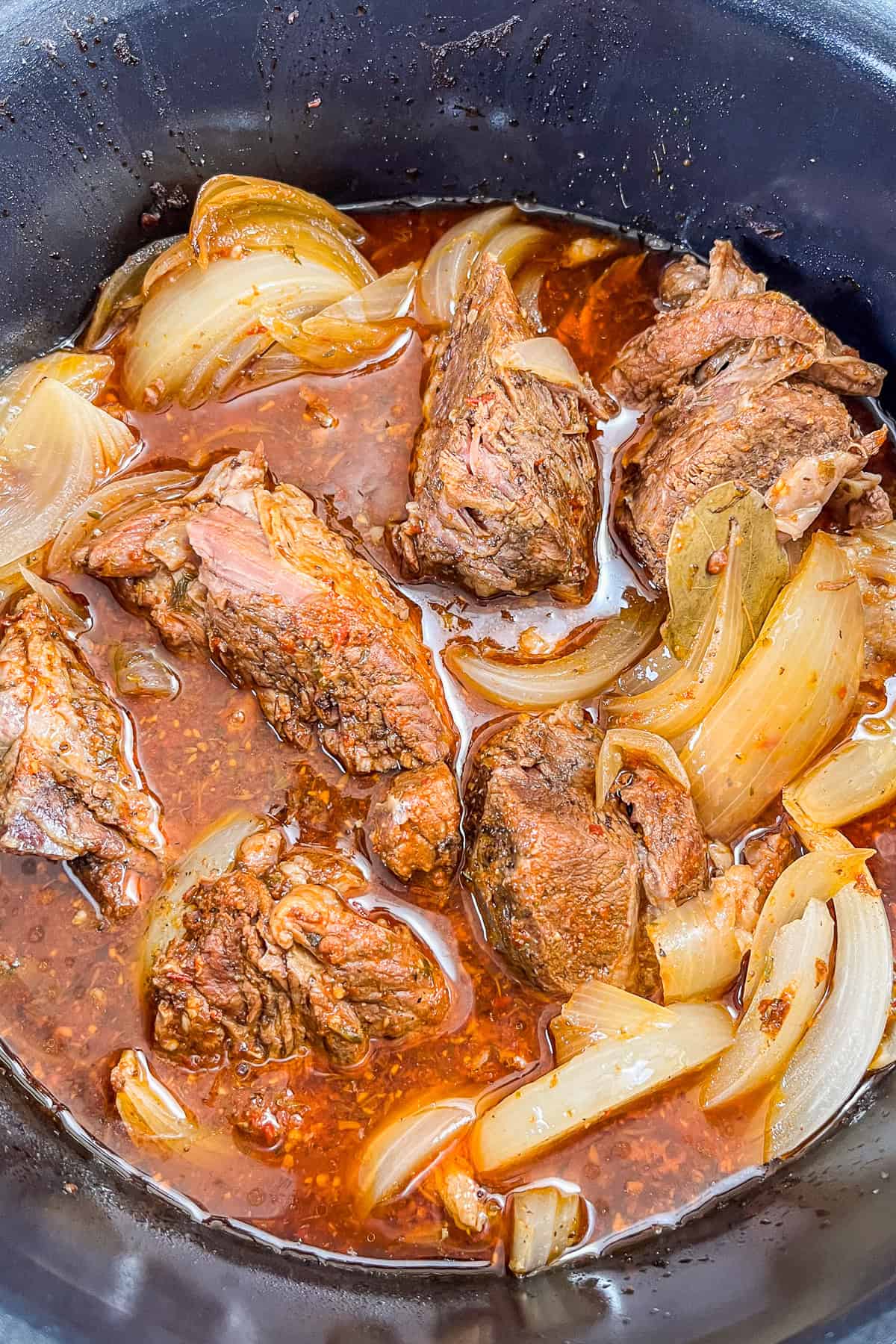 Beef barbacoa with sliced onions in a slow cooker.