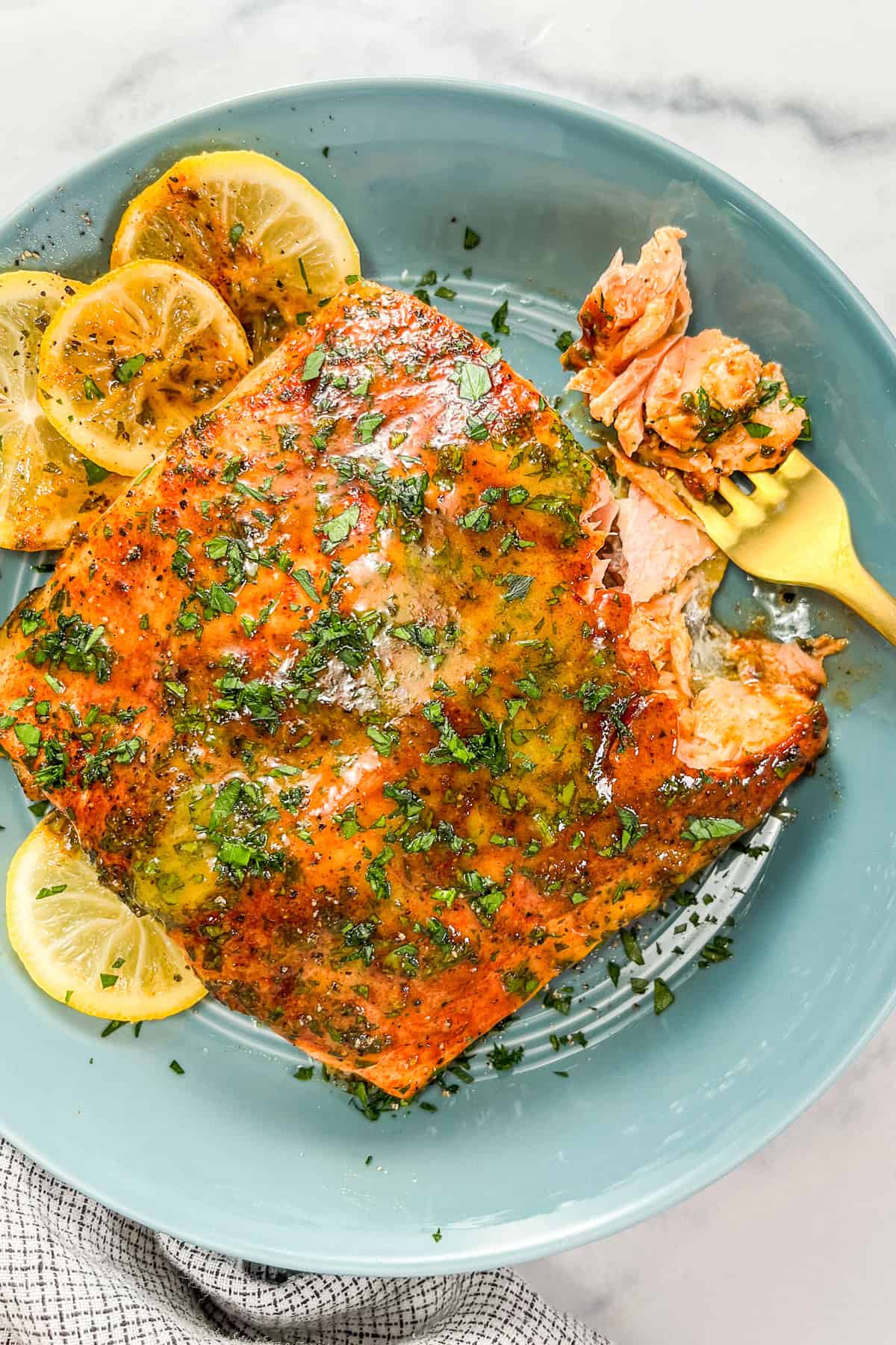 Dijon honey salmon with lemon slices in a blue bowl with a gold fork.