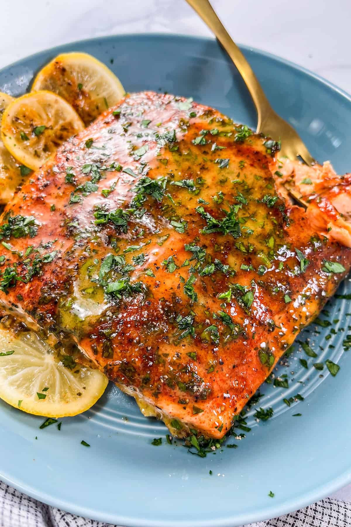 Dijon honey salmon with lemon slices in a blue bowl with a gold fork.