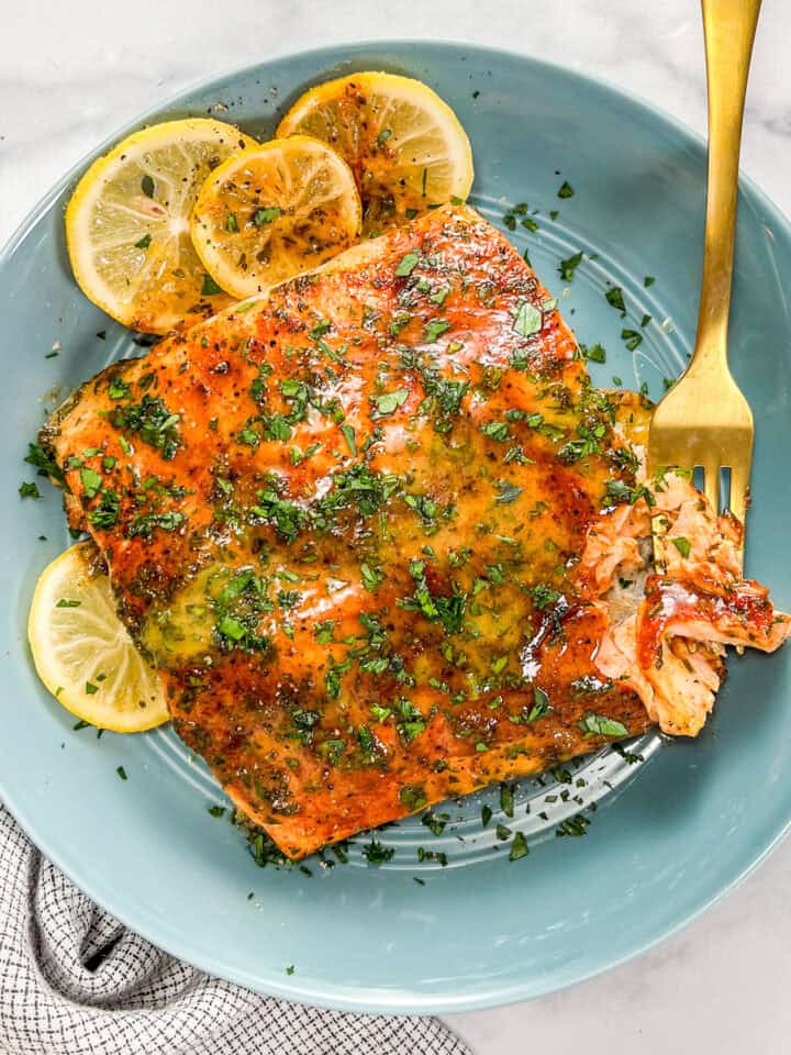 Dijon honey salmon with lemon slices in a blue bowl with a gold fork.