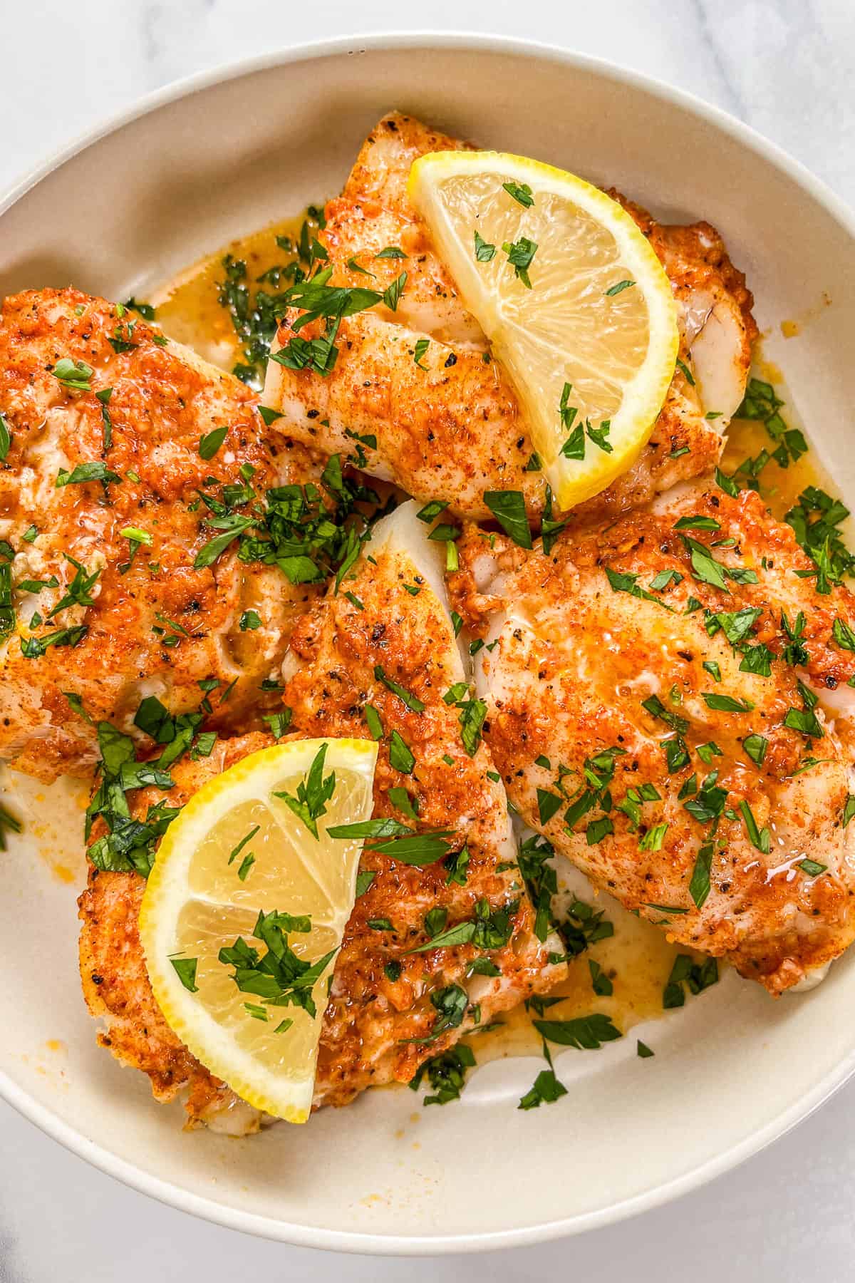 Lemon garlic butter baked cod fillets in a white bowl, topped with lemon slices.
