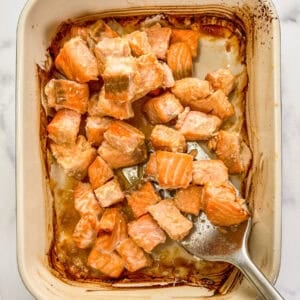 Miso salmon chunks in a baking dish being scooped up with a silver spatula.