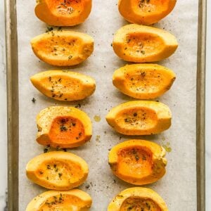 Carnival squash slices on a parchment lined sheet pan topped with oil and herbs.