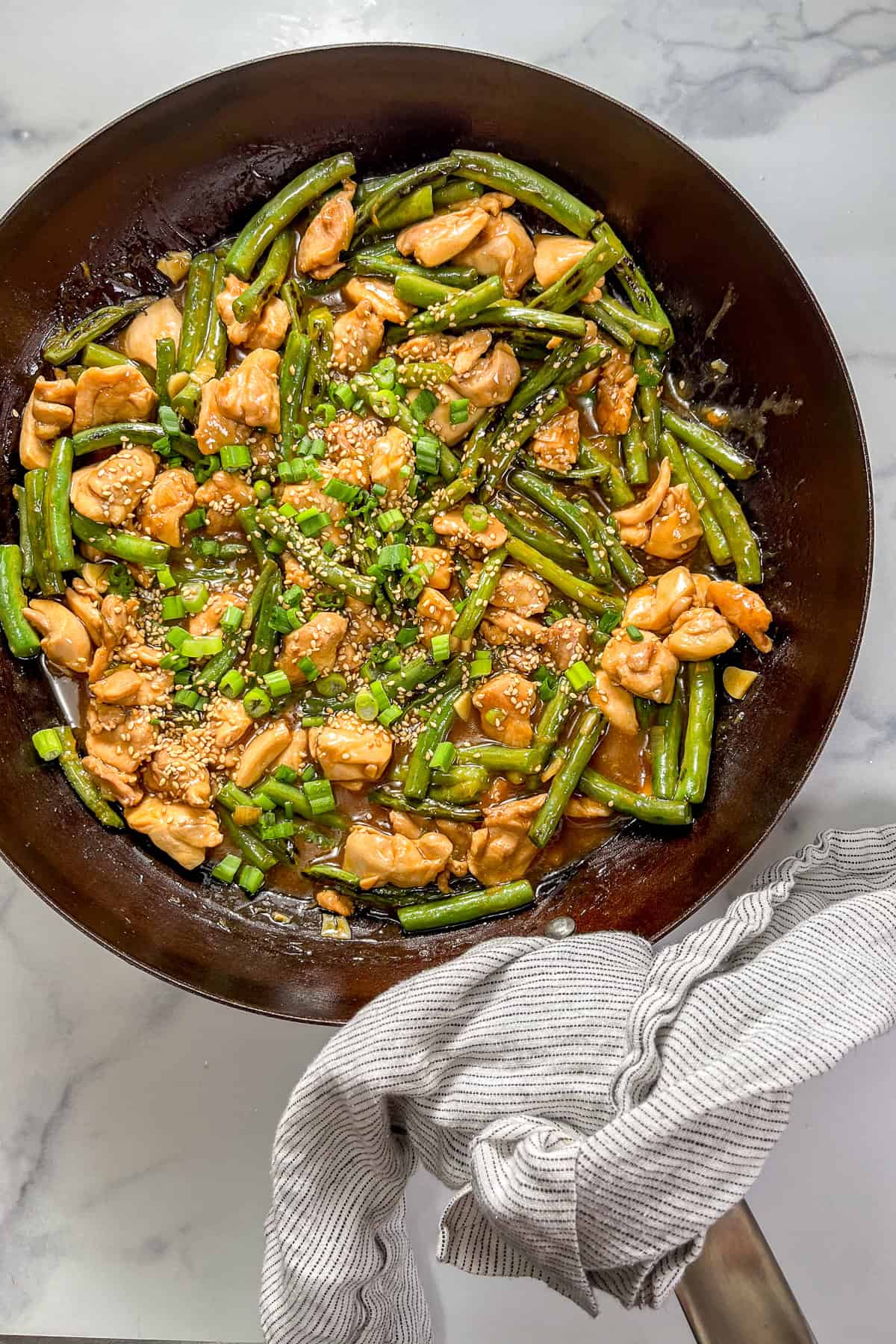 Chicken and green bean stir fry in a large pan wrapped with a towel.