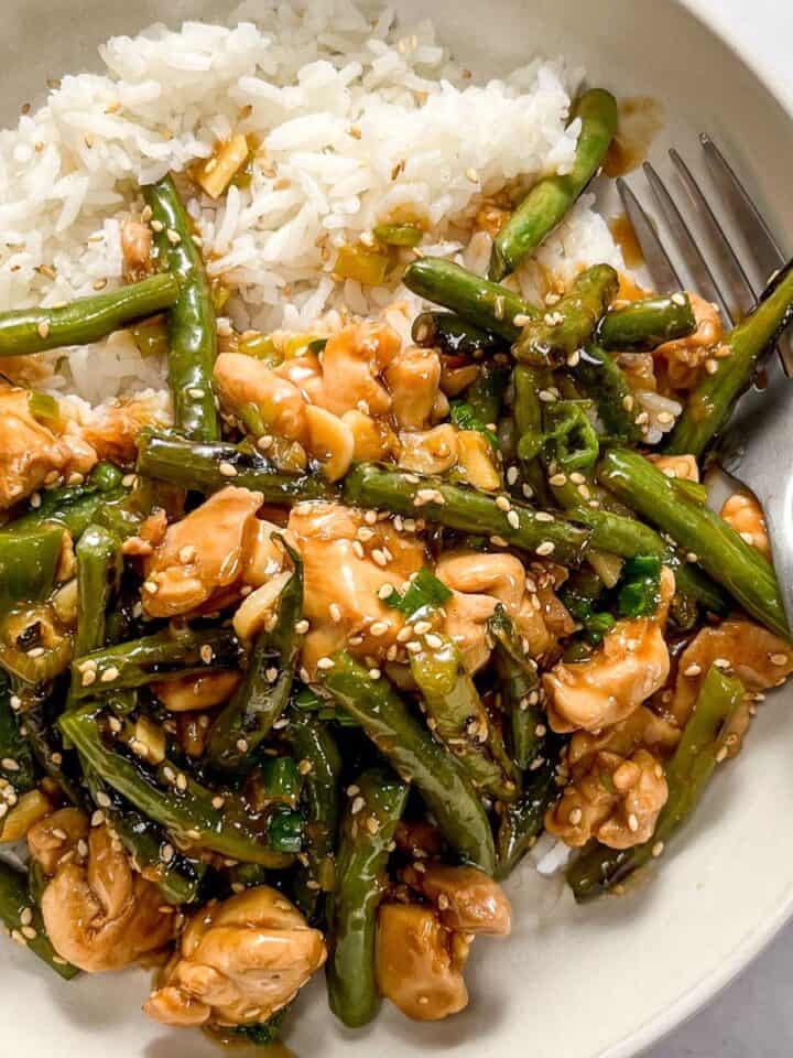 Chicken green bean stir fry with white rice in a white bowl with a silver fork.