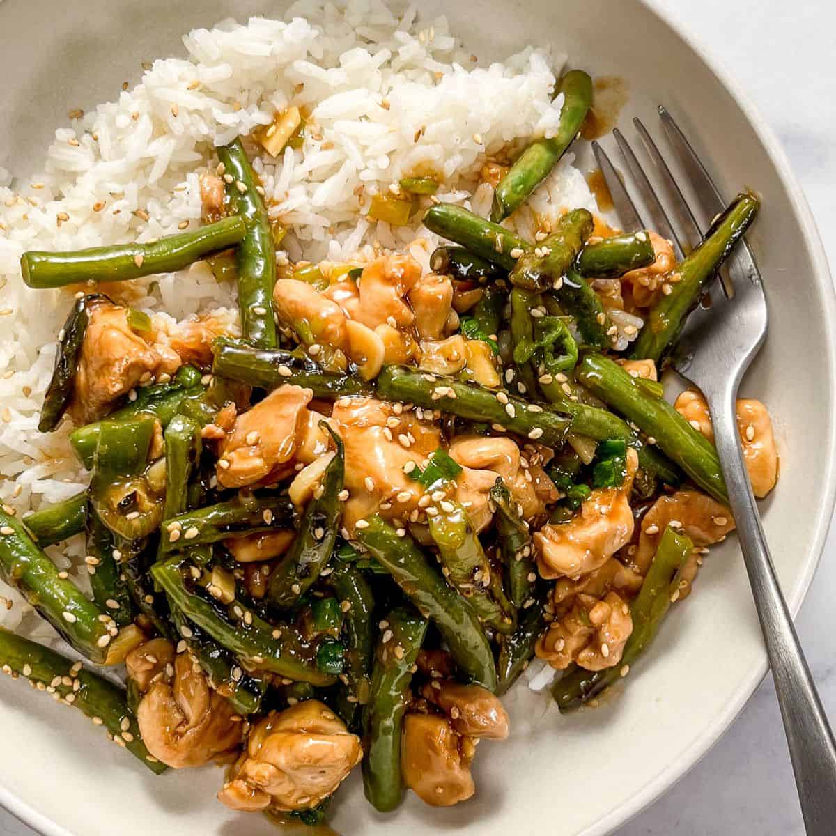 Chicken green bean stir fry with white rice in a white bowl with a silver fork.