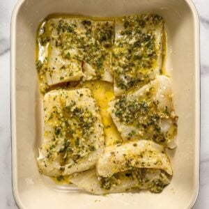 White fish marinating in Greek oil and lemon sauce in a pan.