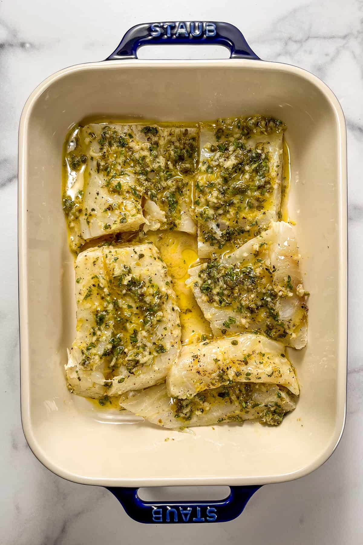 Greek marinade on white fish in a baking dish.