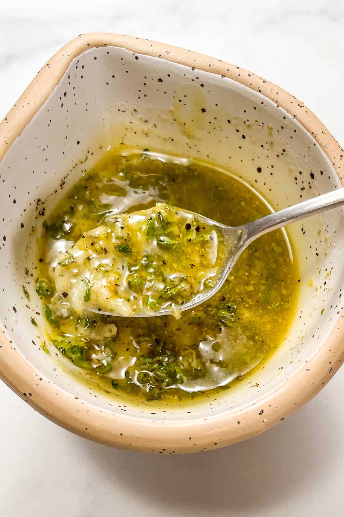 Greek marinade in a speckled bowl with a silver spoon.
