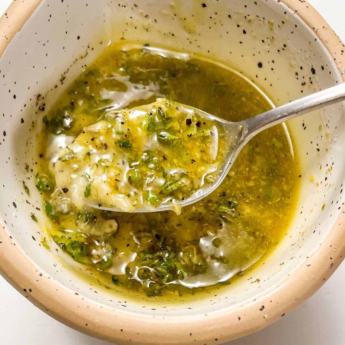 Greek marinade in a speckled bowl with a silver spoon.