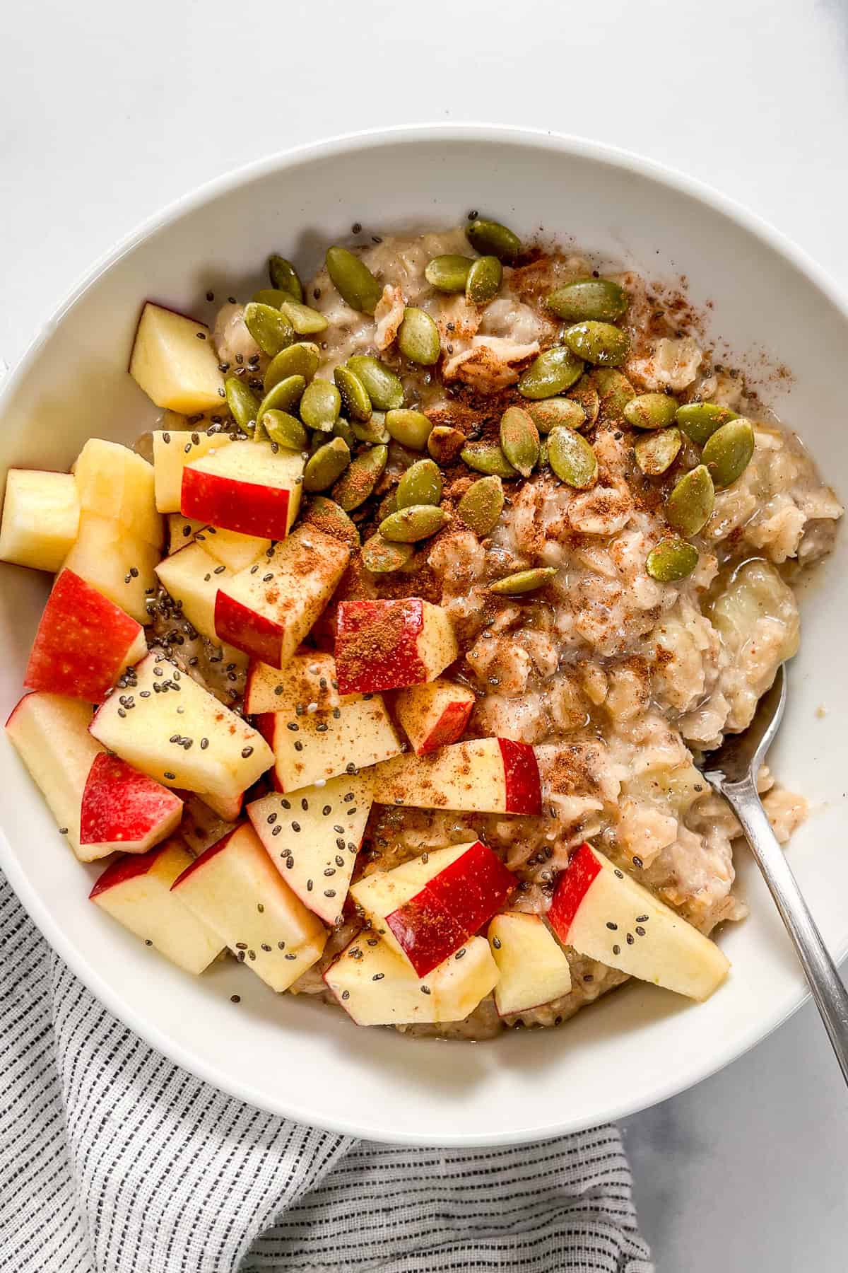 Pumpkin spice oatmeal topped with pepitas, pumpkin spice seasoning, and chopped apples.