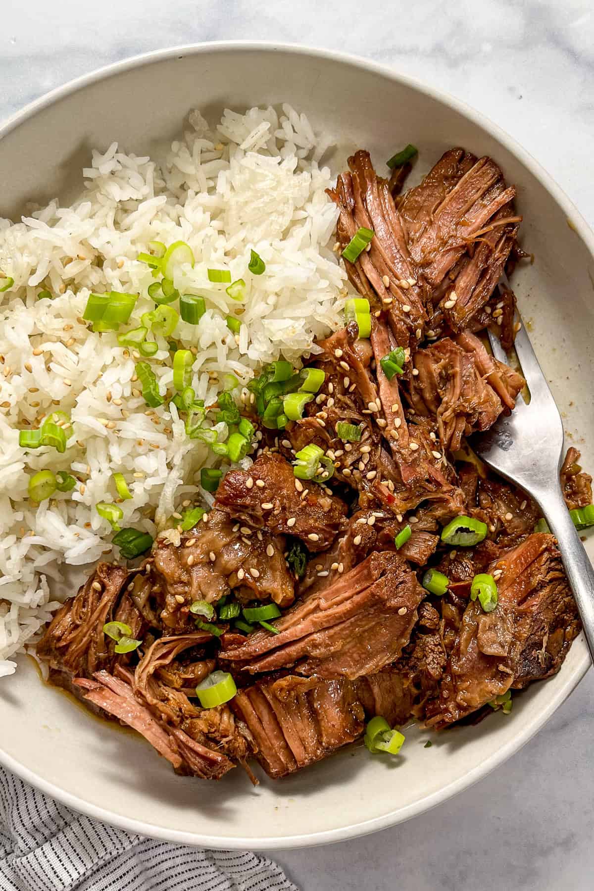 A fork in a bowl of slow cooker beef bulgogi with rice.