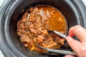 Tongs in a slow cooker of Korean shredded beef.