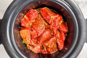 Chunks of beef in a slow cooker with sauce and sliced green onions.
