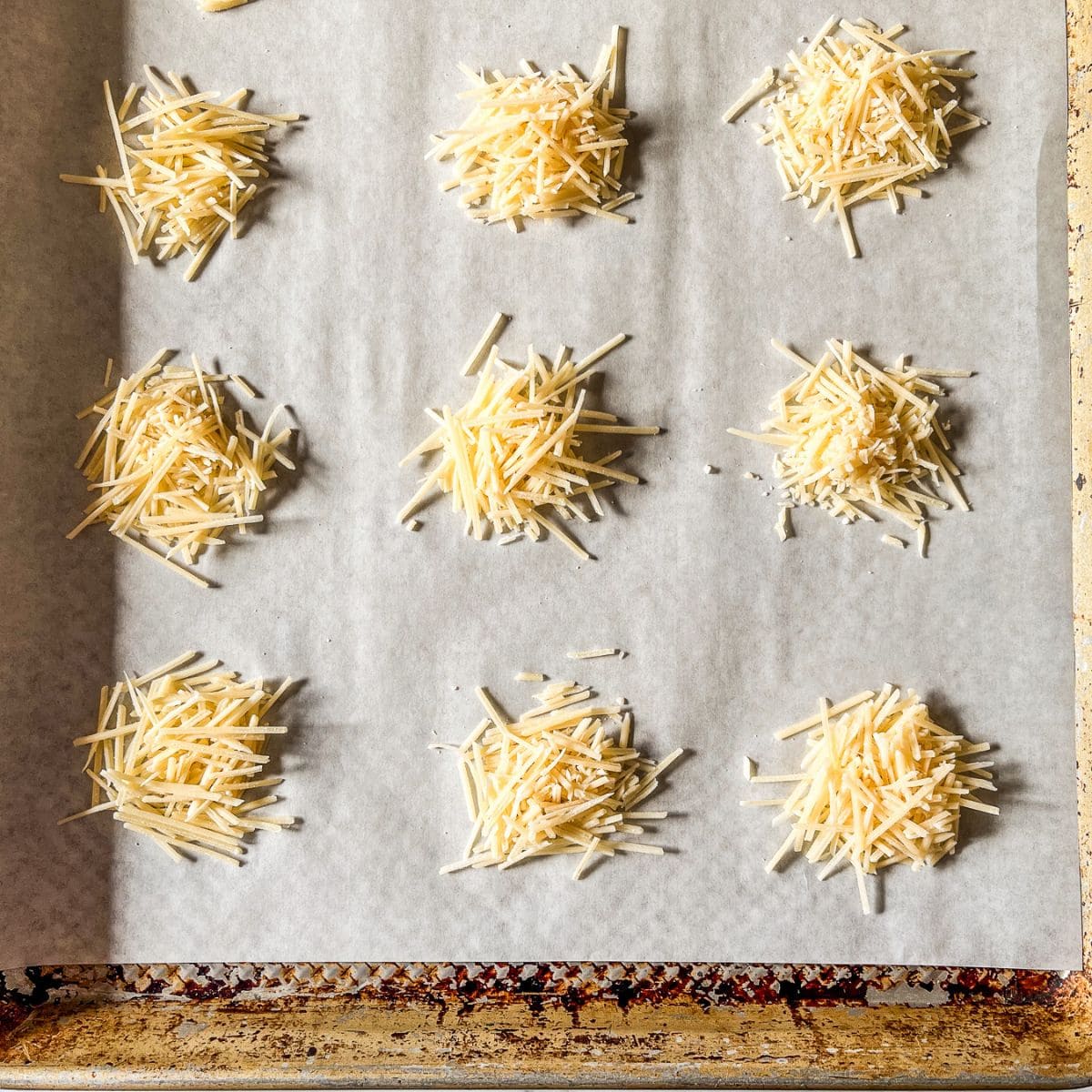 Mounds of parmesan cheese on a parchment lined sheet pan.
