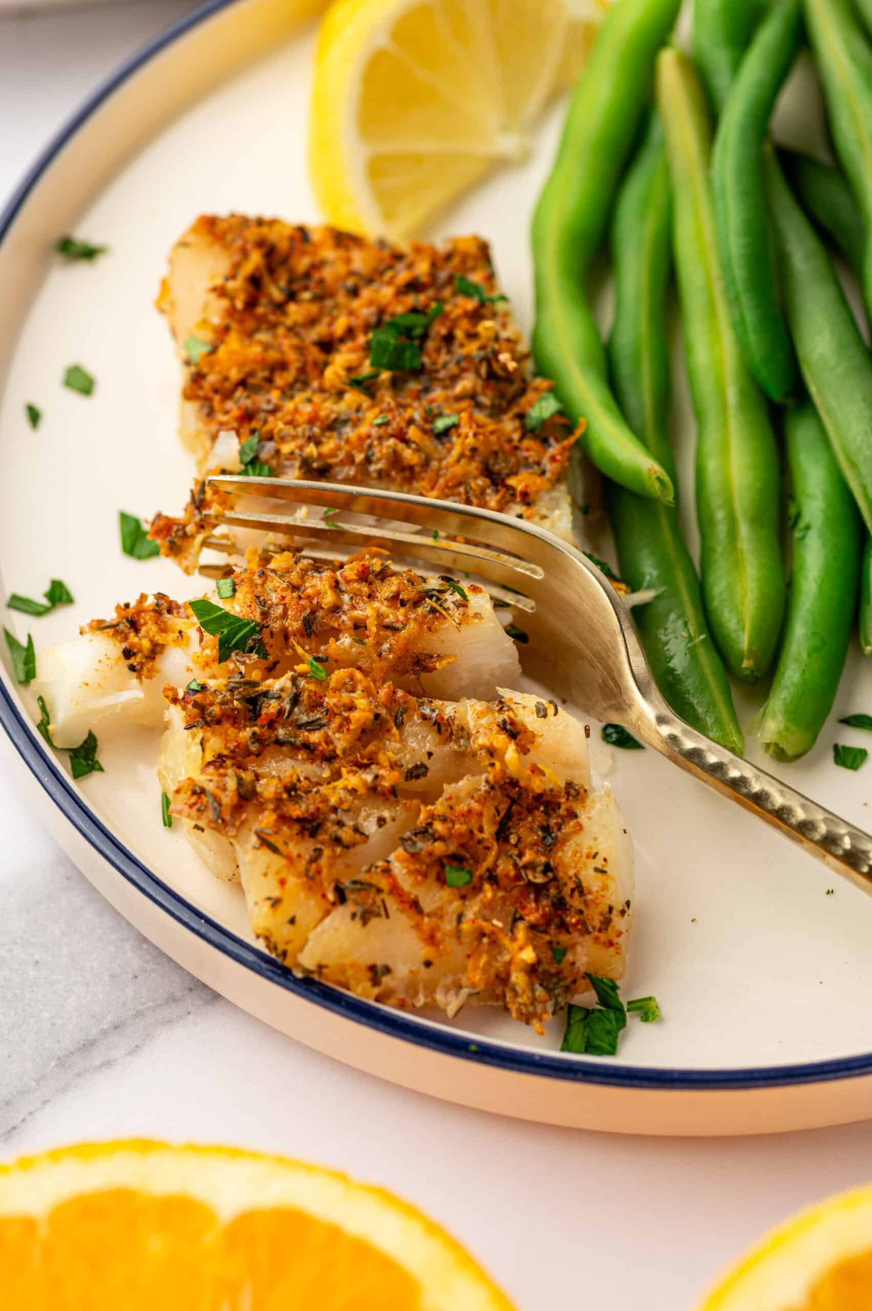 Herb citrus crusted cod on a white plate next to green beans.